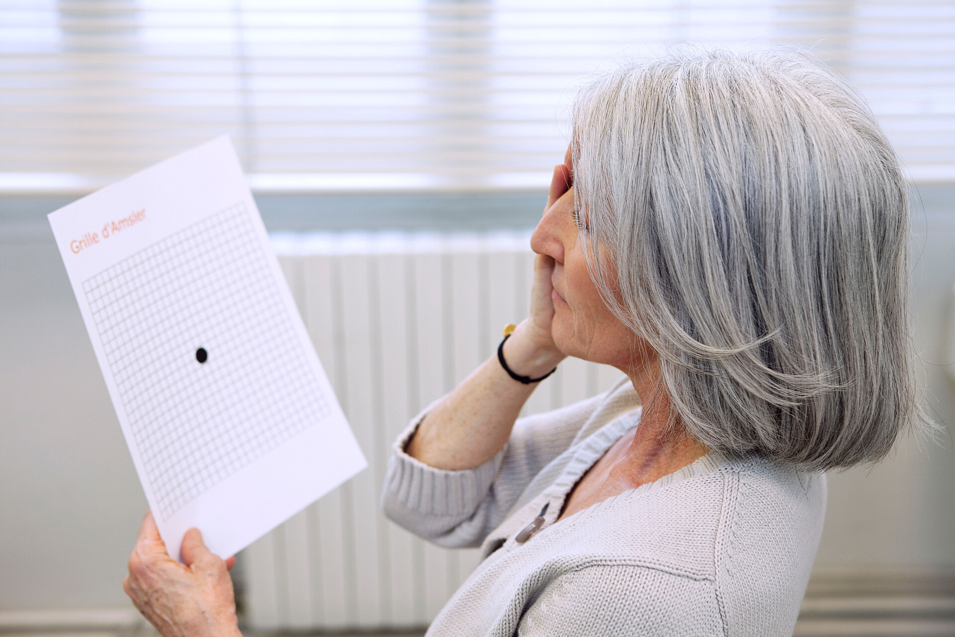 Kvinna håller för ena ögat och tittar på Amsler-testet